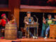 Three cast members pose in front of mismatched tables